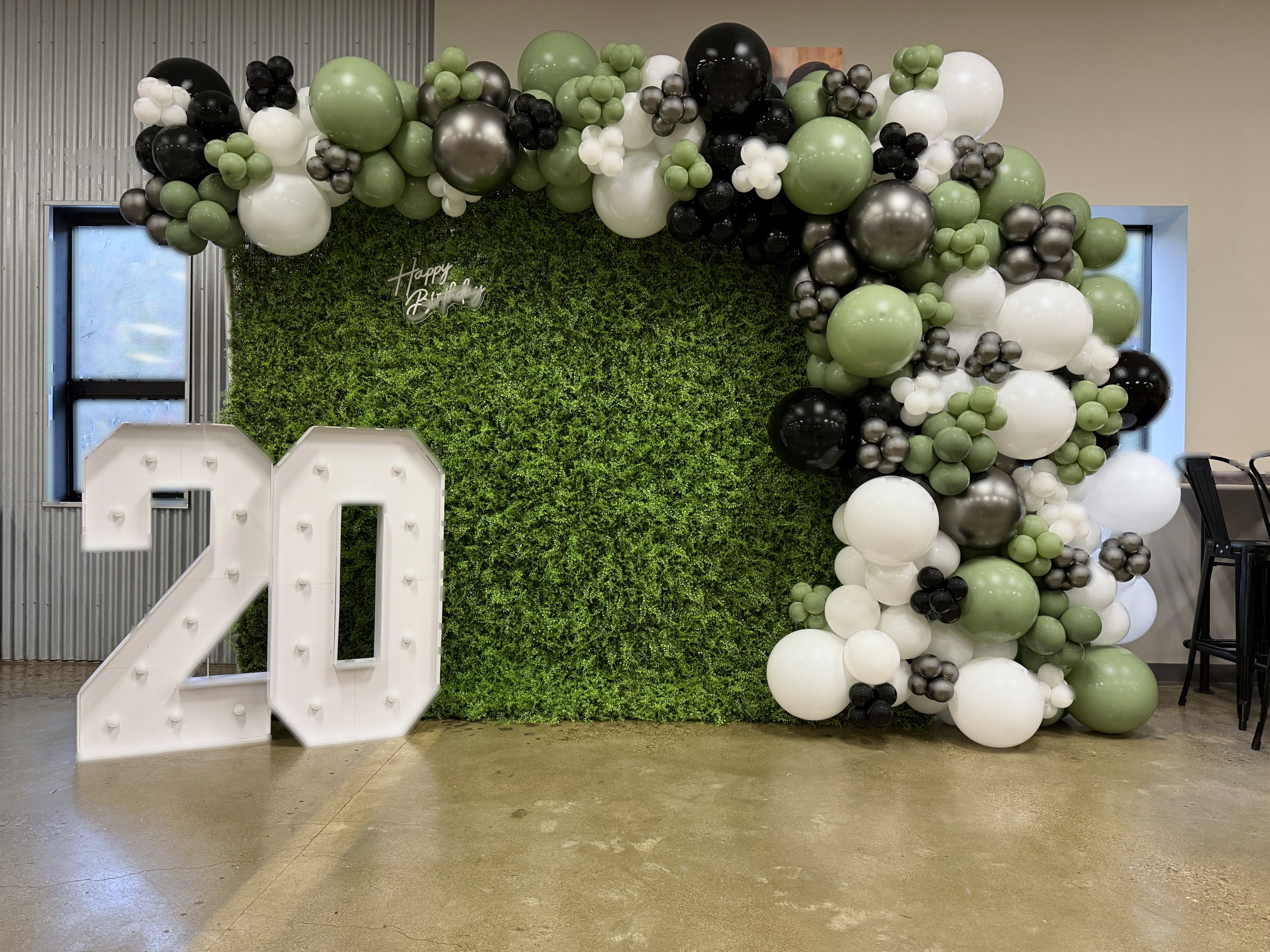 Birthday balloon garland with illuminated numbers on greenery wall