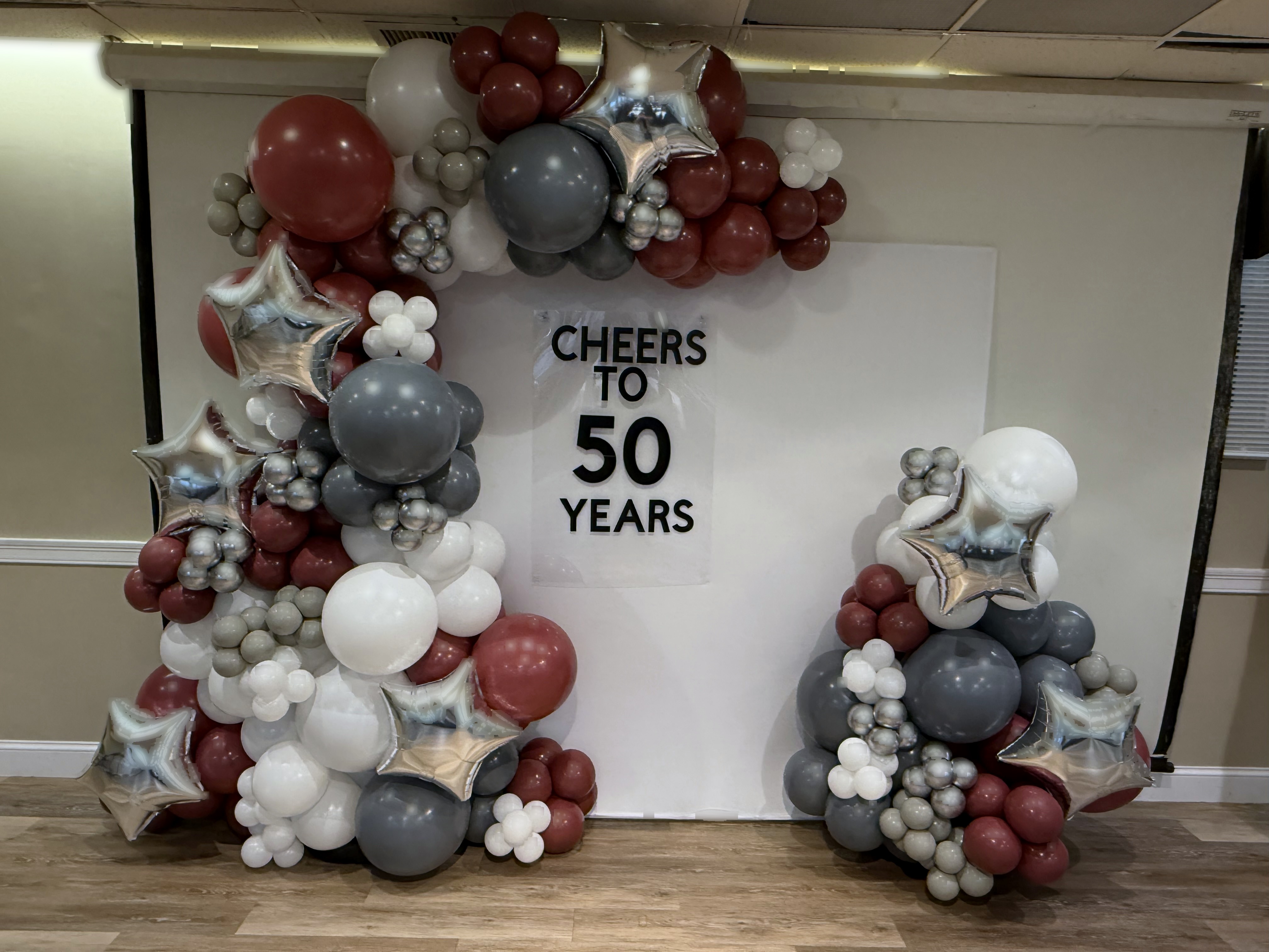 Burgundy, silver, and champagne organic balloon garland framing a 50th birthday celebration wall