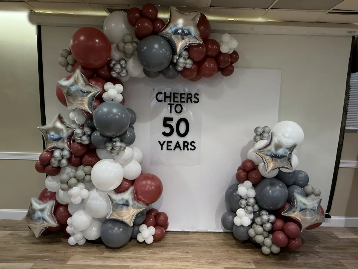 Burgundy, silver, and champagne organic balloon garland framing a 50th birthday celebration wall
