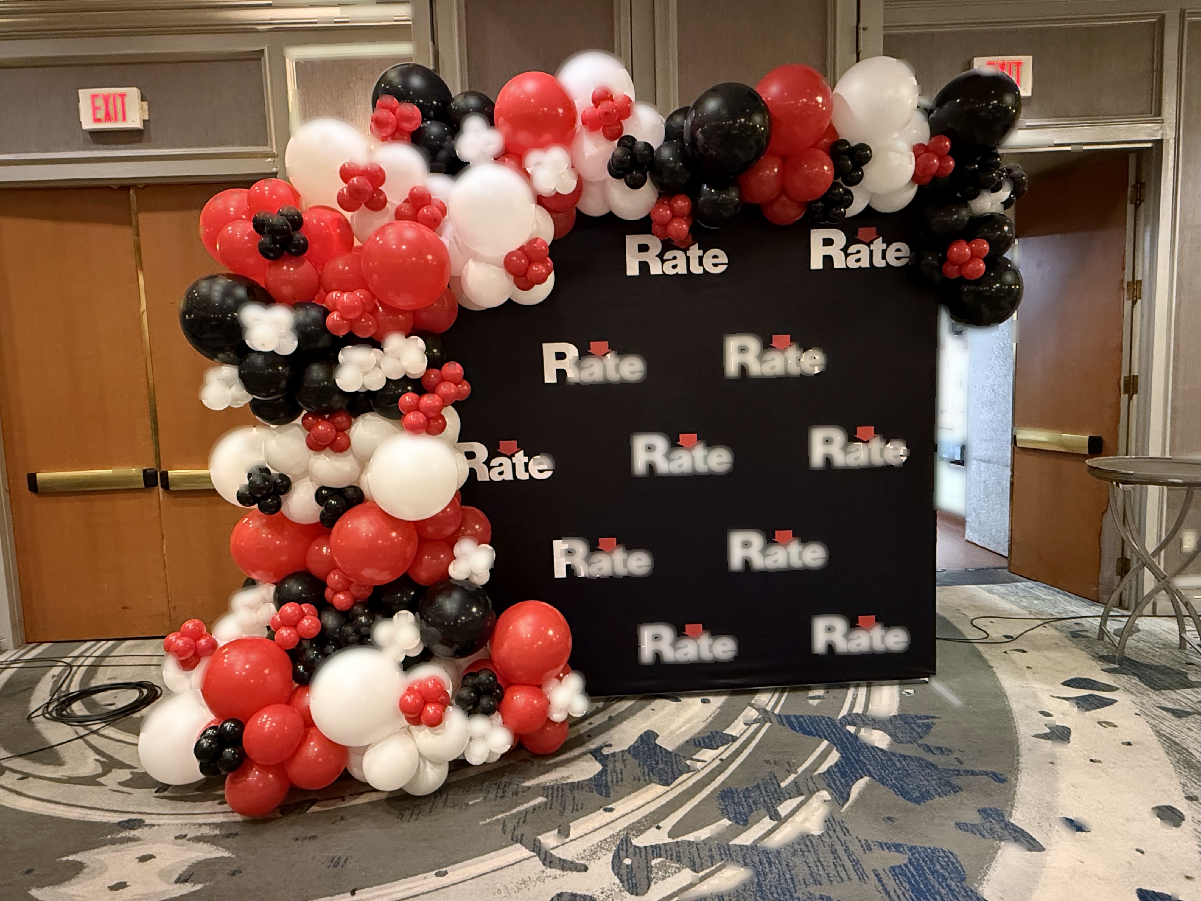 Red, black, and white balloon garland framing a Rate corporate media wall and step-and-repeat backdrop