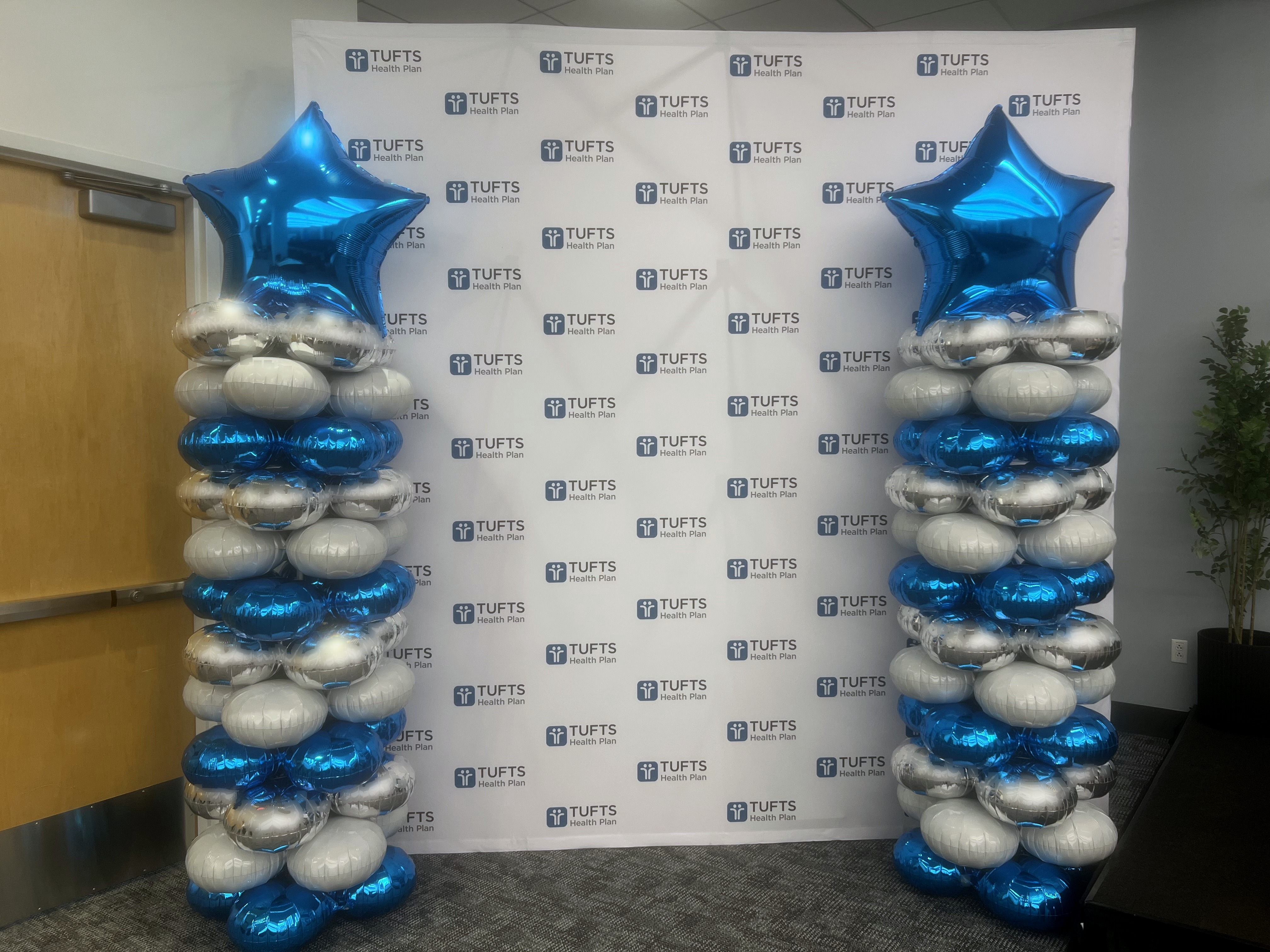 Blue and silver spiral balloon columns with star toppers flanking a Tufts Health Plan corporate step-and-repeat